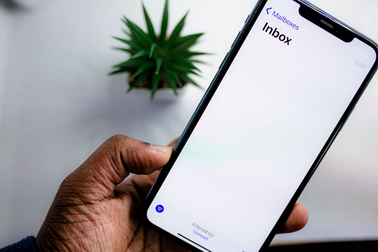 Detailní pohled na displej smartphonu s otevřenou e-mailovou schránkou, který drží dospělá ruka.